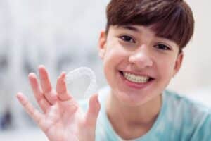 Teen Boy holding invisalign in hand showing his smile