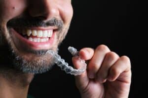 Man smiling while holding clear Invisalign aligner tray near his mouth.